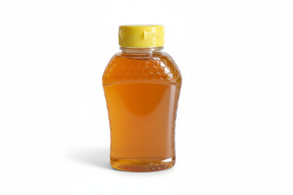 A clear plastic honey bottle filled with golden honey, featuring a textured honeycomb pattern on the upper half and a yellow screw cap, sitting on a light-colored surface.