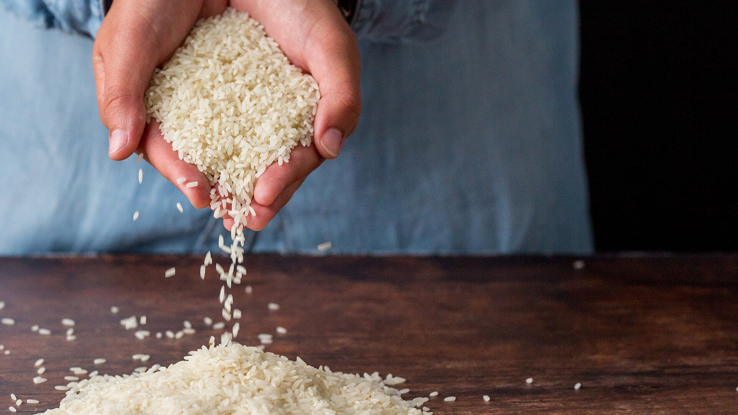 Person pouring white rice from hand onto a wooden surface