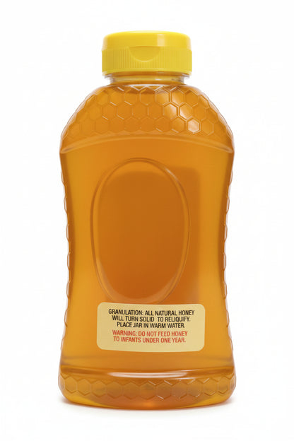A plastic squeeze bottle of honey with a yellow cap, filled with golden honey, on a textured light gray surface.